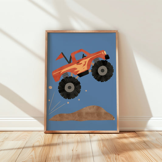 A framed art print featuring a stylized orange monster truck jumping over a brown hill on a blue background, leaning against a white wall on a light wood floor.