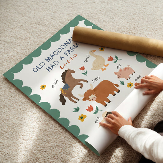 A child's hands are unrolling a printed educational poster about farm animals on a beige carpet, with a brown cardboard mailing tube placed on top.