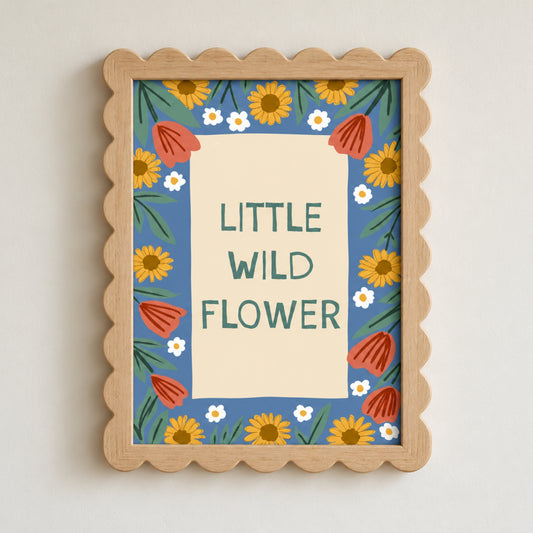 A framed wall art print with a scalloped light wood frame. The artwork features the text 'LITTLE WILD FLOWER' in green on a cream background, surrounded by a blue border decorated with yellow sunflowers, red poppies, and small white flowers.