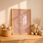 A framed nursery art print featuring a white line art illustration of a ballerina's tutu dress on a dusty pink background, styled on a wooden dresser next to plush toys in a woven basket.