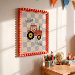 A framed children's wall art print hangs on a wall in a sunlit room. The print shows a red tractor on a light blue and white checkerboard background with the word 'BRUM' twice.