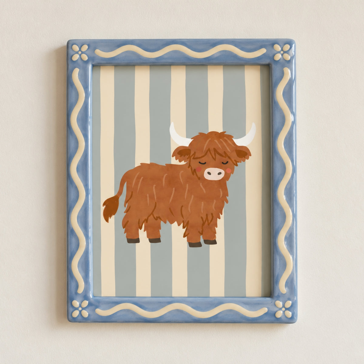 A framed wall art print featuring a brown shaggy Highland cow illustration on a light blue and cream striped background, set in a blue frame with cream wavy borders.