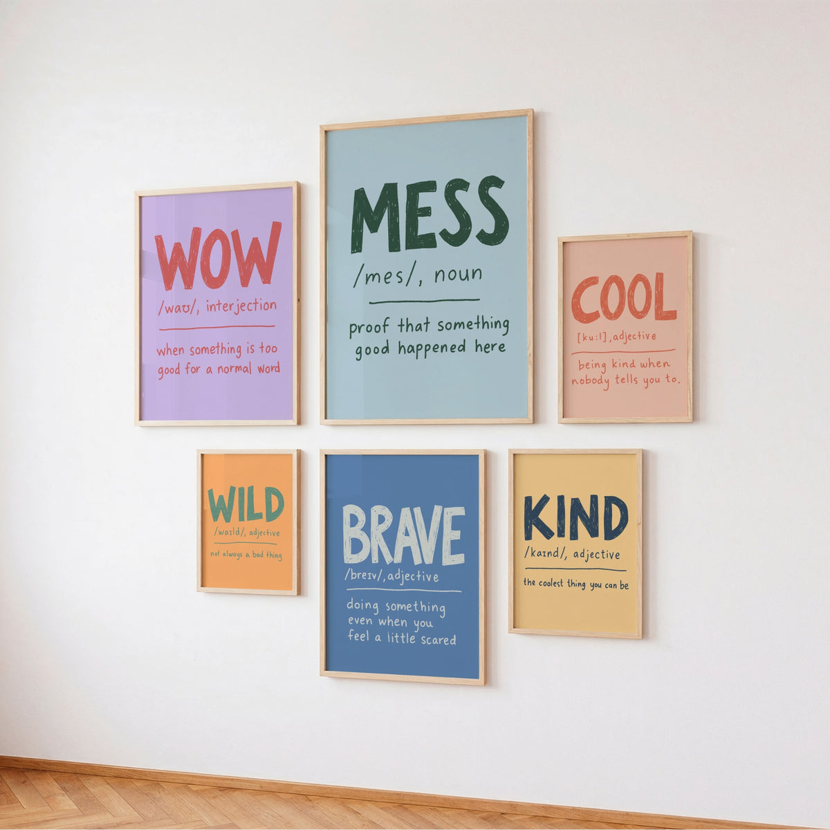 Six framed typography wall art prints with colorful educational-style words and definitions, arranged on a white wall above a wood floor.