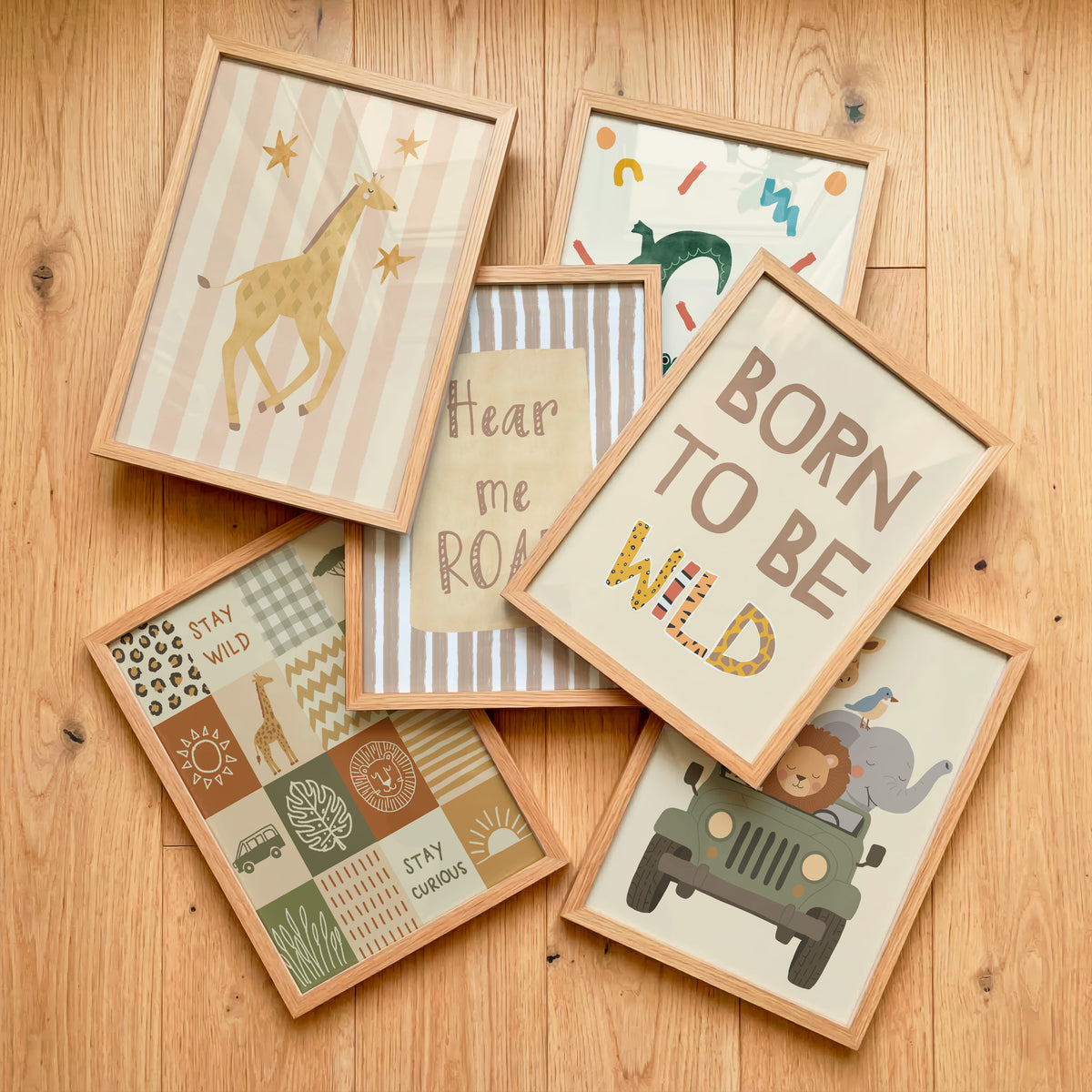 Six framed nursery art prints with light wood frames are arranged on a light wood floor. The prints feature safari-themed illustrations and playful text including 'BORN TO BE WILD', 'Hear me roar', 'STAY WILD', and 'STAY CHER'.