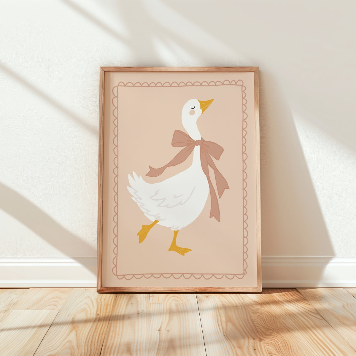 A framed art print featuring a cute white goose with a brown bow and yellow beak/legs, leaning against a white wall on a light wood floor with soft window shadows.
