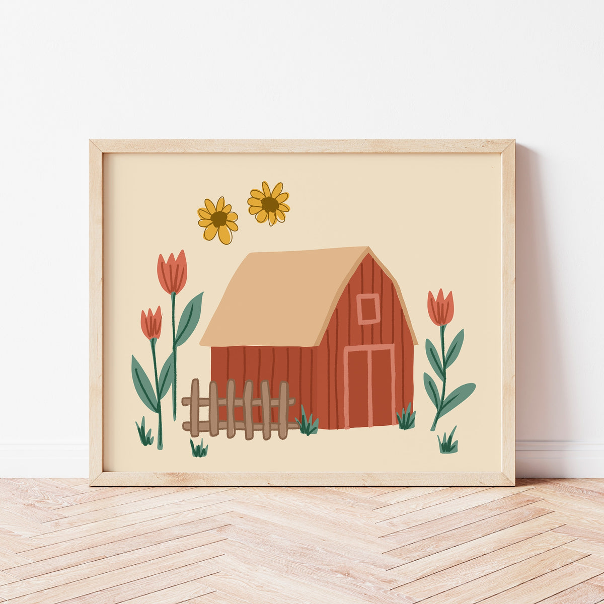 A framed art print featuring a whimsical barn illustration with yellow sunflowers and red tulips, leaning against a white wall on a light wood herringbone floor.