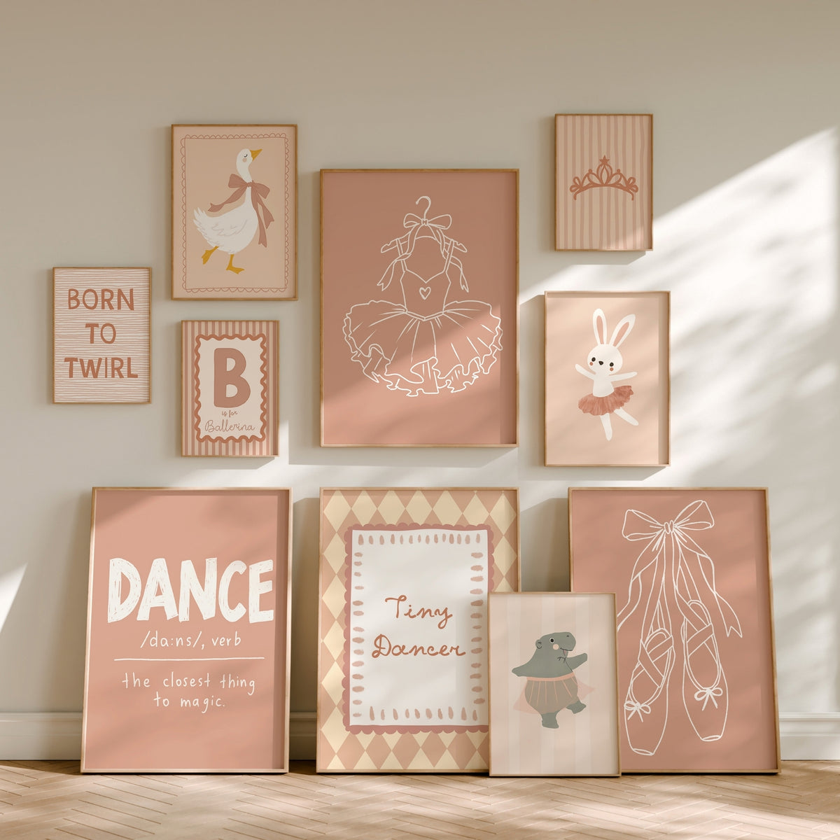 A coordinated set of framed nursery wall art prints arranged on a beige wall above a light wood floor. The prints feature ballet-themed illustrations and text, including a ballerina, bunny in tutu, ballet shoes, tiara, duck, and phrases such as 'BORN TO TWIRL' and 'DANCE is the closest thing to magic.