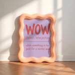A wavy peach-colored picture frame leaning against a white wall on a wooden floor, displaying a purple insert with the word 'WOW' and a dictionary-style definition in red text.