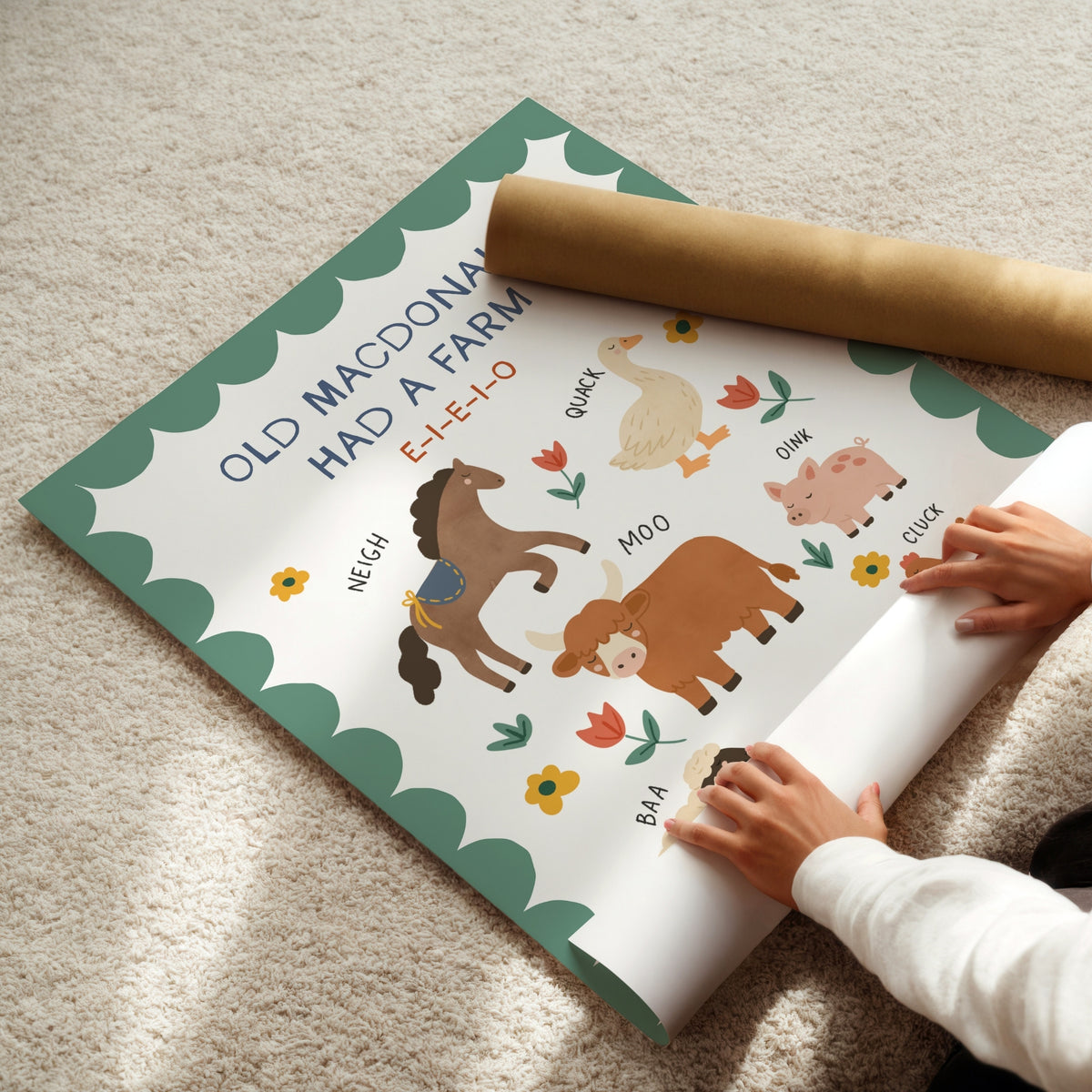 A child's hands are unrolling a printed educational poster about farm animals on a beige carpet, with a brown cardboard mailing tube placed on top.