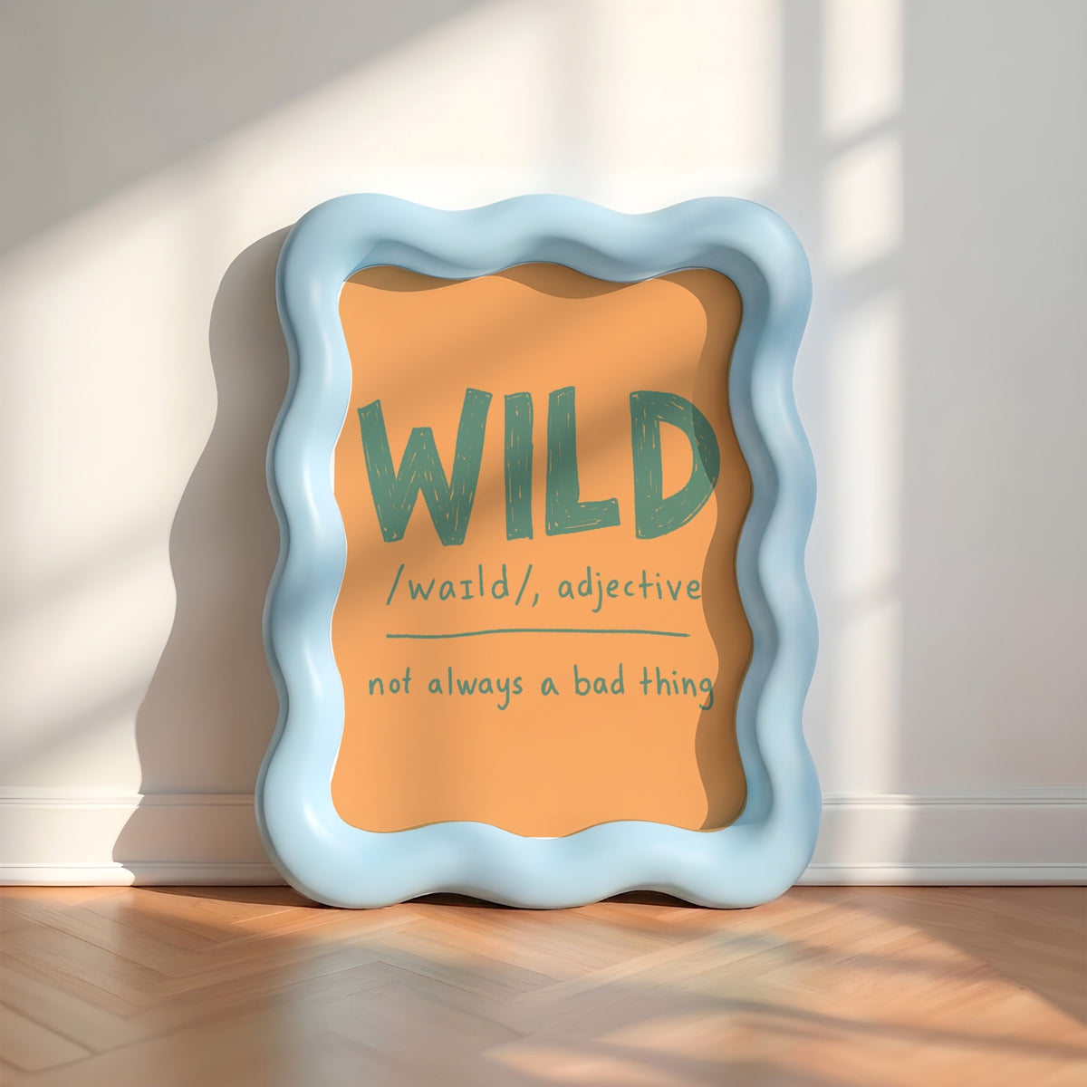 A wavy light blue picture frame leaning against a white wall on a wood floor, displaying an orange sign with the word 'WILD' and a dictionary-style definition.