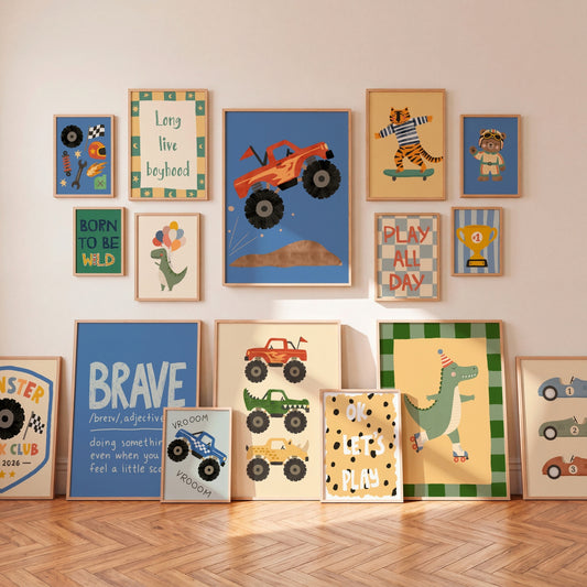 A styled collection of framed children's wall art and prints displayed on a beige wall above a herringbone wood floor. The prints feature retro-style illustrations of race cars, a jumping orange monster truck, a tiger on a skateboard, a dinosaur roller skate, and motivational text like 'Long live keybord', 'BORN TO BE WILD', and 'PLAY ALL DAY'.