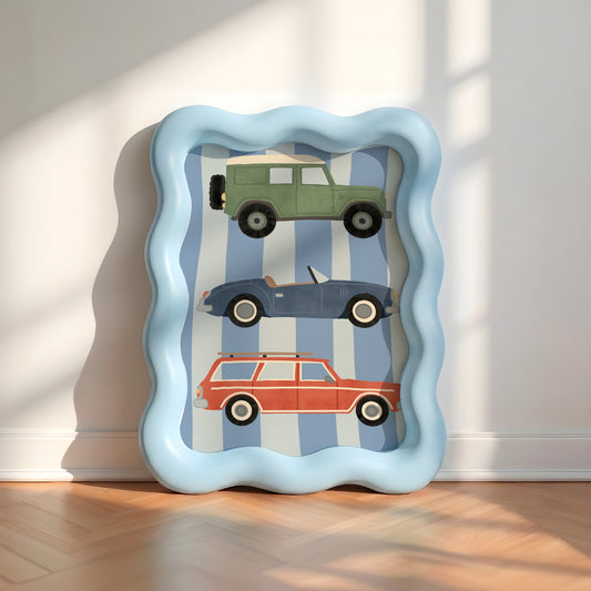 A square wavy-edged framed art print leaning against a white wall on a wooden floor. The print features three vintage toy cars (green station wagon, blue convertible, and red station wagon) on a blue and white striped background.