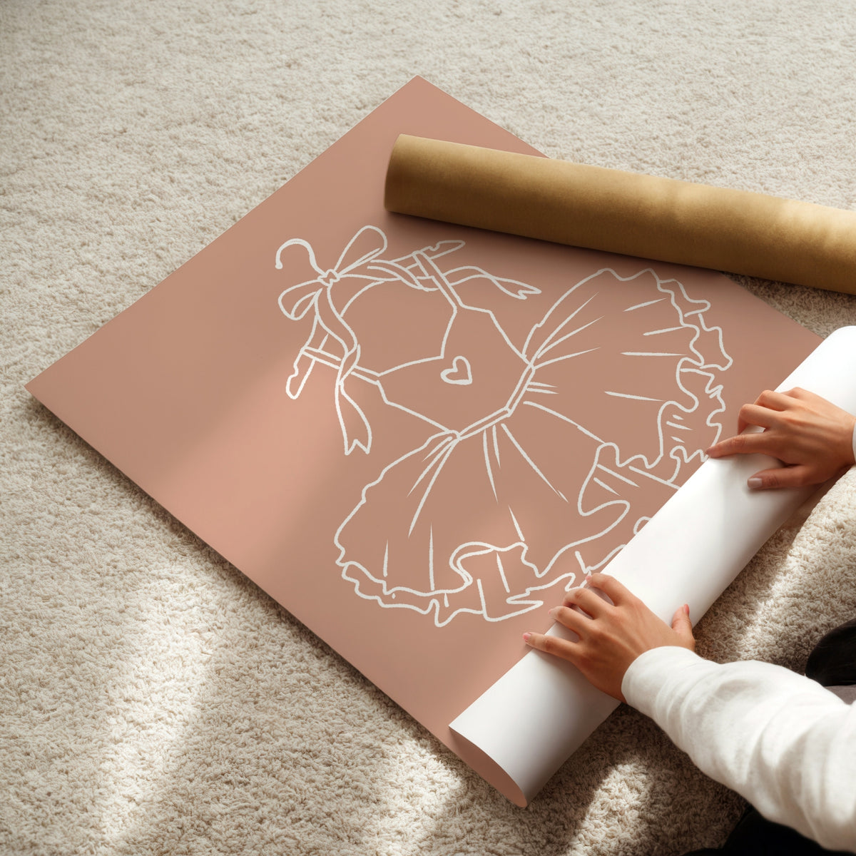 A person's hands are shown unrolling a large sheet of dusty rose pink vinyl floor decals with a white line-art design of a ballerina, next to a roll of matching pink decals on a beige carpet.