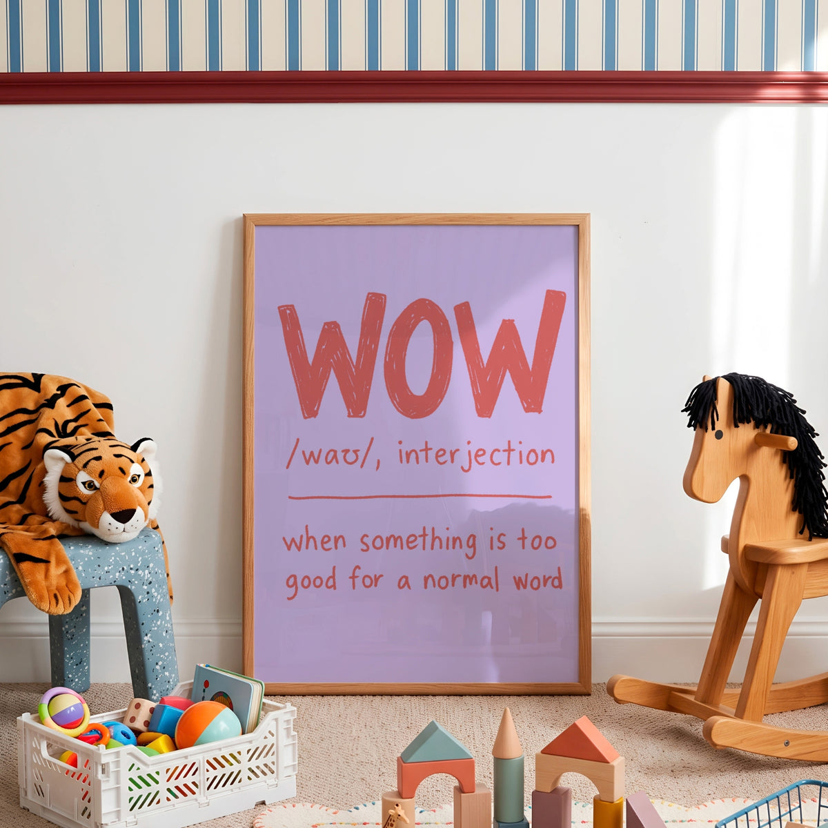 A framed nursery art print leaning against a white wall in a child's playroom. The print features a light purple background with the word 'WOW' in large coral-red letters and a definition below.