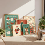A set of framed Christmas-themed art prints leaning against a wall in a styled room. The prints include a 'Santa Starter Pack' design, alphabet letters with holiday motifs, Rudolph the Red-Nosed Reindeer, Santa, and 'Ho Ho Ho' patterns.