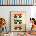 A framed vertical art print featuring three colorful monster truck illustrations, displayed on a carpeted floor in a styled children's room with toys, a striped wall, and a rocking horse.
