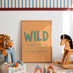 A framed children's wall poster with the word 'WILD' and its pronunciation and definition, styled in a nursery or playroom with a wooden rocking horse, a stuffed tiger, and toys on the floor.
