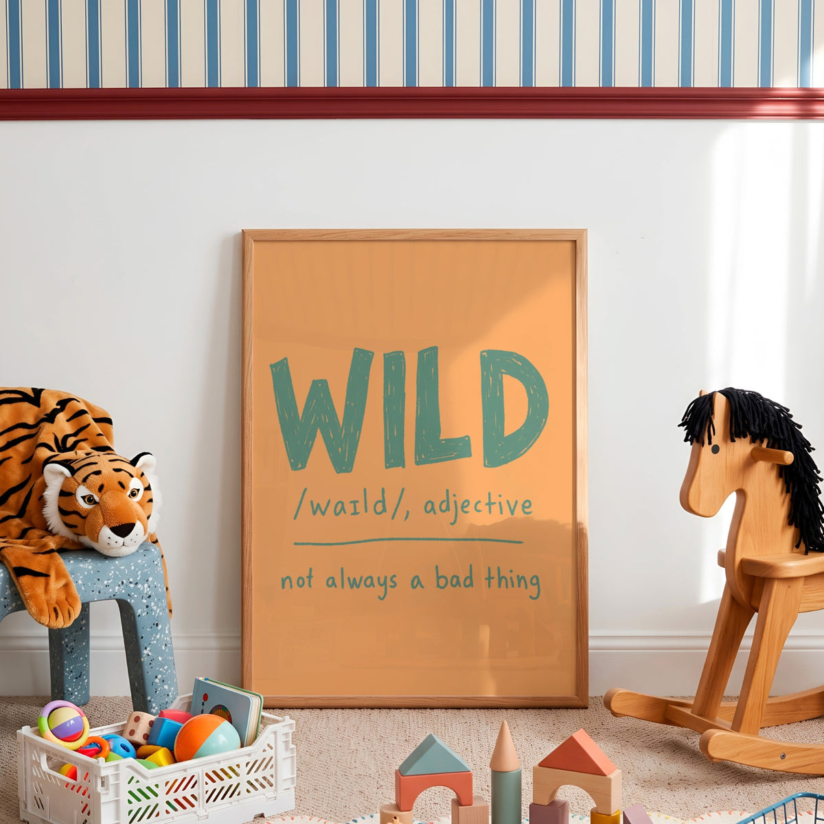 A framed children's wall poster with the word 'WILD' and its pronunciation and definition, styled in a nursery or playroom with a wooden rocking horse, a stuffed tiger, and toys on the floor.