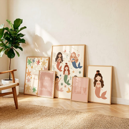Five mermaid nursery prints leaning against a wall beside a plant, showing mermaid friends, tails and "Wanna play mermaids?" quote