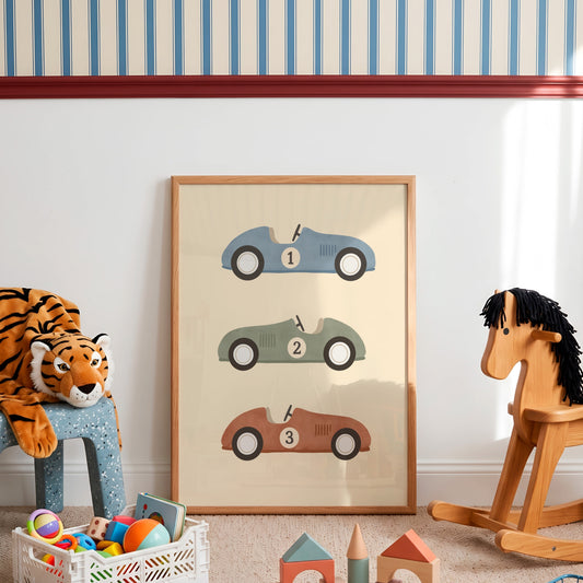 A framed vertical art print featuring three numbered vintage race cars in blue, green, and brown on a cream background, styled in a children's room next to a plush tiger, a wooden rocking horse, and toy blocks.