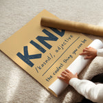 A person unrolling a large kraft paper poster on a beige carpet, with a matching rolled sheet placed on top. The poster features the word 'KING' in large dark blue letters and the phrase 'king /kānd/, adjective the coolest thing you can be' in smaller dark blue text.