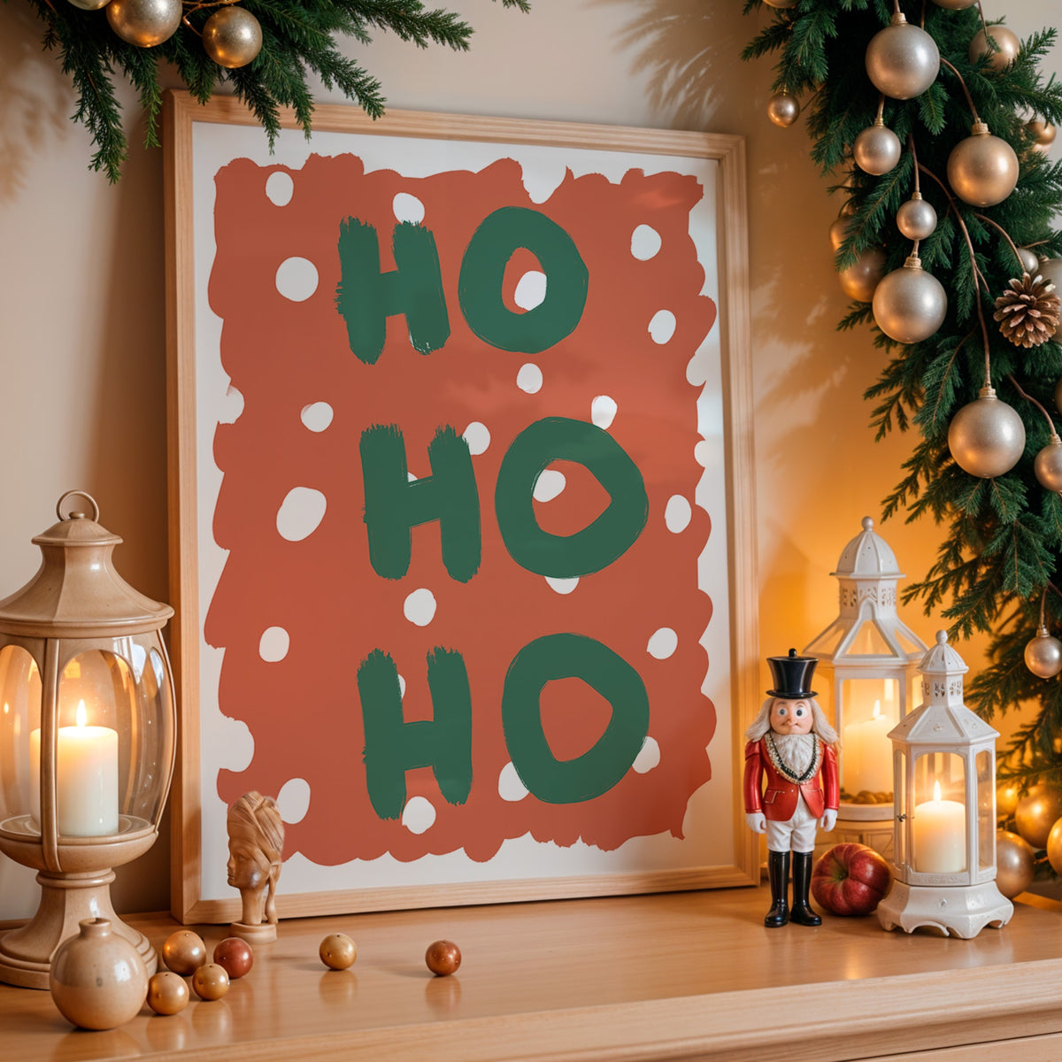 A framed Christmas art print with the words 'HO HO HO' in green brushstrokes on a terracotta background with white polka dots, styled on a wooden mantel with candles, ornaments, and a nutcracker.