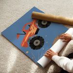 A person is unrolling a large wall mural or poster featuring a stylized orange fire truck with black wheels on a blue background, placed on a beige carpet. A brown cardboard roll is visible behind the mural.