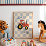 A framed children's wall art print leaning against a white wall in a playroom. The print shows a red tractor on a beige and light blue checkerboard background with the word 'BRUM' twice.