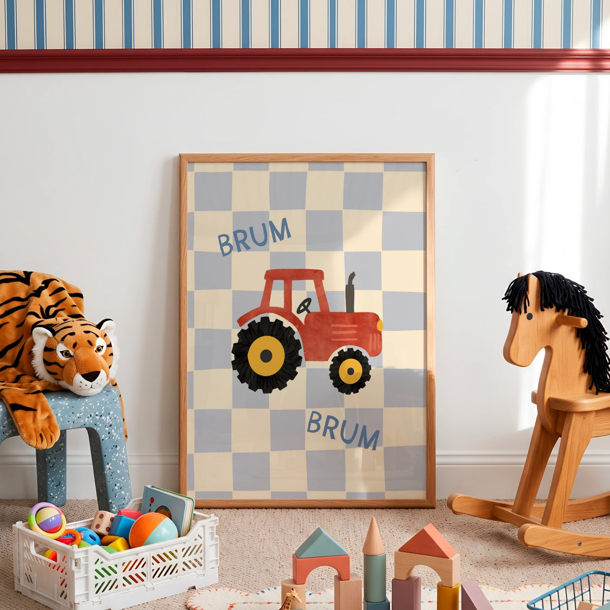 A framed children's wall art print leaning against a white wall in a playroom. The print shows a red tractor on a beige and light blue checkerboard background with the word 'BRUM' twice.