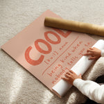Hands unrolling cool definition print from kraft shipping tube, showing terracotta lettering on blush