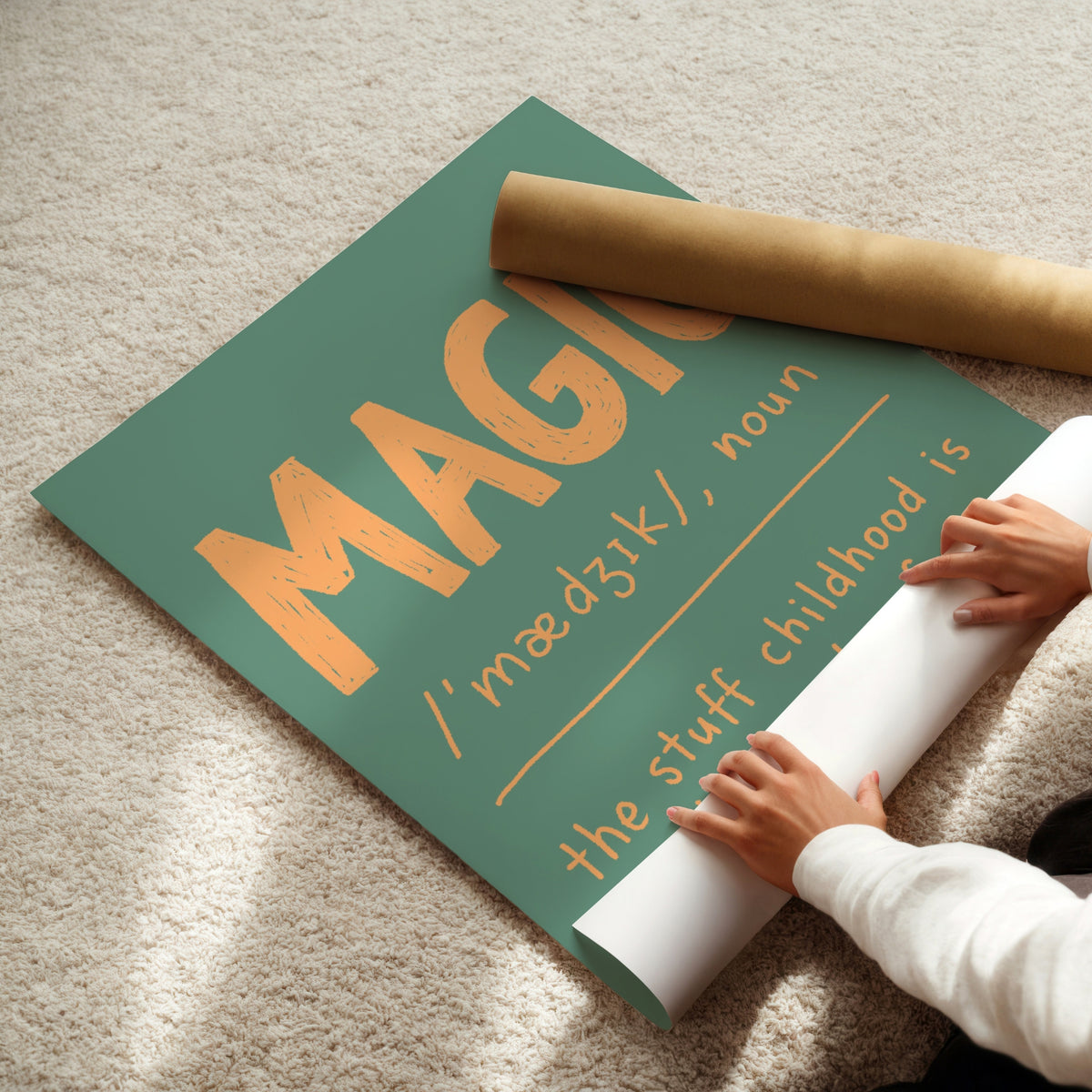 A person unrolls a large decorative poster on a beige carpet. The poster has a muted teal-green background with large orange text reading 'MAGIC' and smaller orange text below.