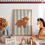 A framed children's wall art print featuring a brown Highland cow on a striped background, displayed in a styled nursery or playroom with toys, a rocking horse, and a plush tiger.