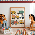 A framed children's wall art print featuring colorful construction vehicles, displayed in a styled nursery or playroom with toys, a rocking horse, and a stuffed tiger.