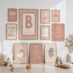 A styled nursery wall display featuring multiple framed ballet-themed prints in soft blush, beige, and terracotta tones, arranged above and below a light wood floor with toys and decor.