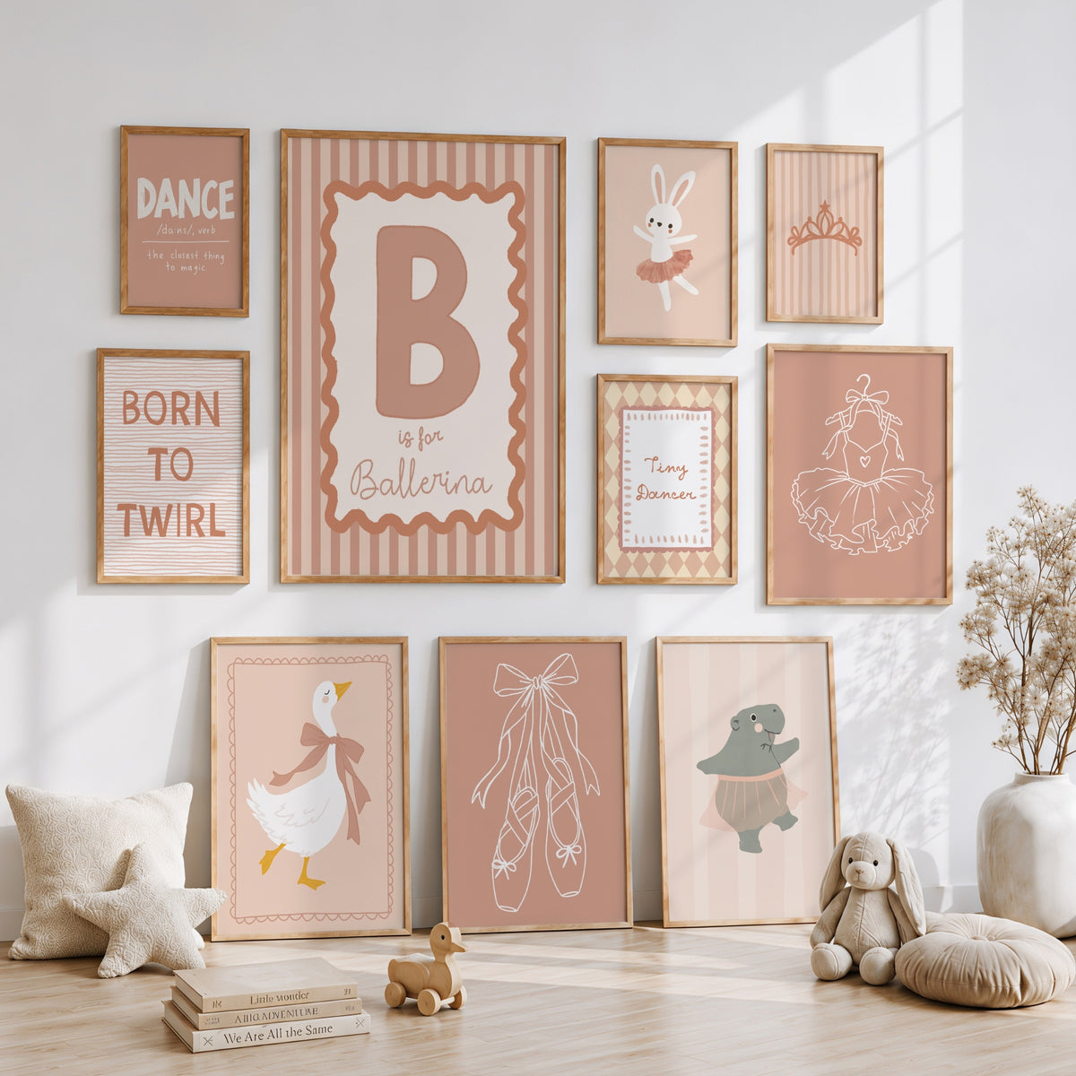 A styled nursery wall display featuring multiple framed ballet-themed prints in soft blush, beige, and terracotta tones, arranged above and below a light wood floor with toys and decor.