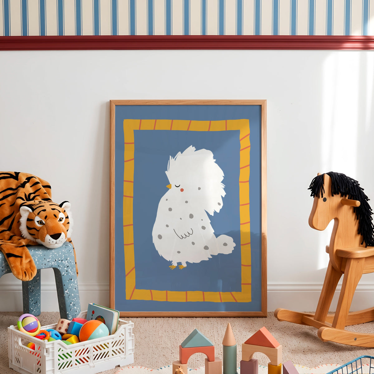 A framed art print featuring a whimsical white fluffy chicken on a blue background with a yellow border, styled in a child's playroom next to a wooden rocking horse and a plush tiger.