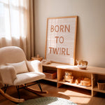 A styled nursery corner with a cream boucle rocking chair, a light wood console shelf with toys, and a framed letter board reading “BORN TO TWIRL” against a warm beige wall.