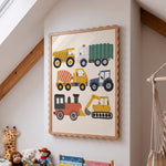 A framed children's wall art print featuring colorful construction vehicles, hanging on a white wall in a child's room with toys and a macrame hanging visible.
