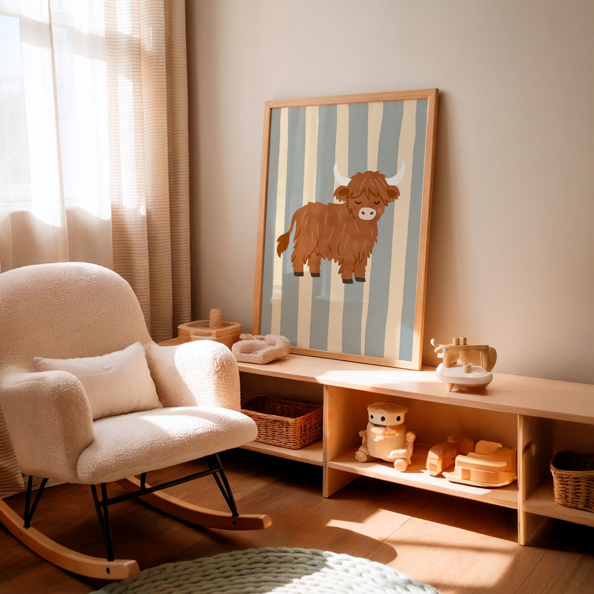 A framed vertical art print featuring a brown cow on blue and cream stripes, styled in a warm, sunlit nursery next to a cream-colored rocking chair and a wooden storage bench.