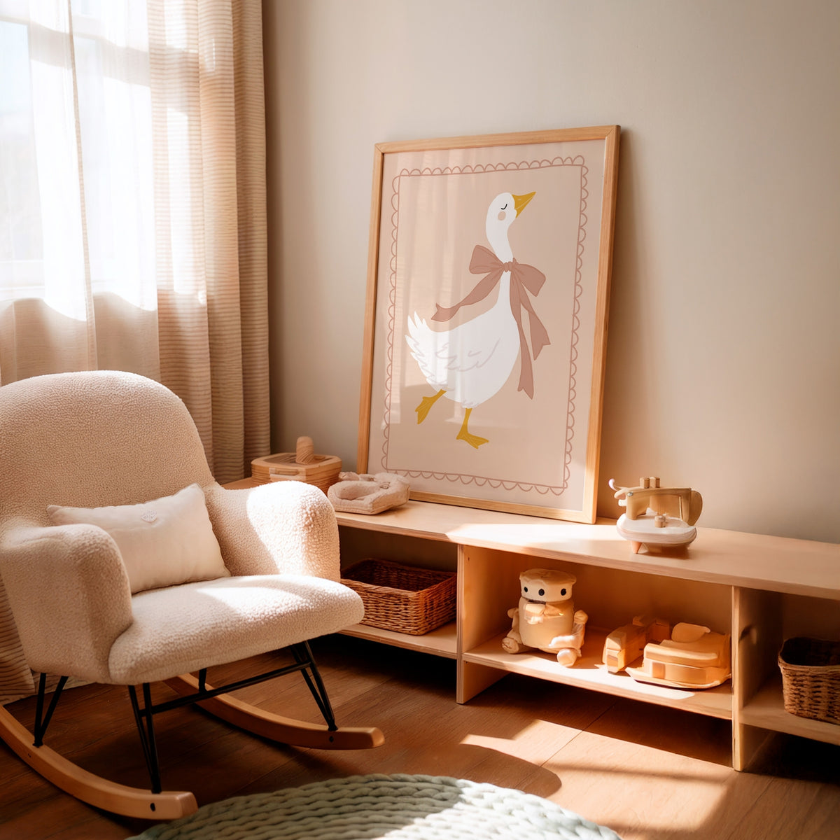 A framed art print of a white duck with a brown bow tie hanging on a beige wall in a softly lit nursery. The room features a cream-colored boucle rocking chair, a light wood toy shelf with toys, and warm natural sunlight streaming through sheer curtains.