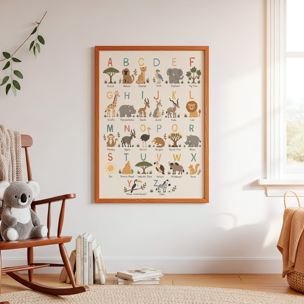 A framed children's alphabet art print featuring safari animals and letters, displayed on a white wall in a styled nursery setting with a rocking chair, plush toy, and window.