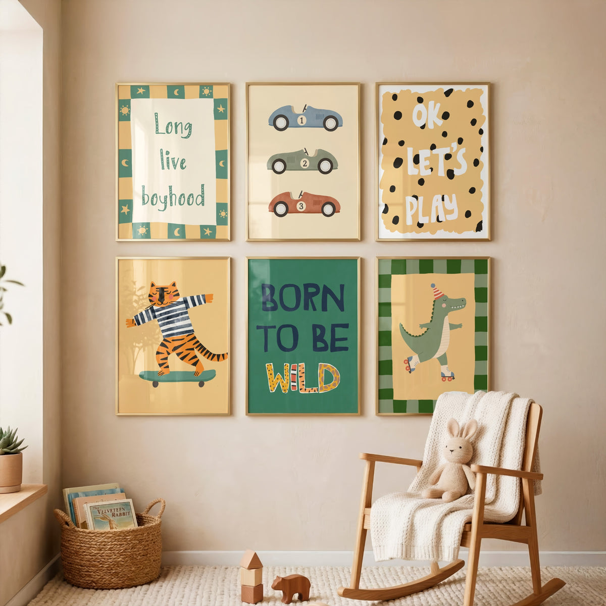 A styled children's room corner showing six framed wall art prints arranged on a beige wall above a wooden rocking chair with a white blanket and stuffed bunny. The prints feature playful illustrations and text including 'Long live boyhood,' 'OK LET'S PLAY,' 'Born to be wild,' and a dinosaur design.