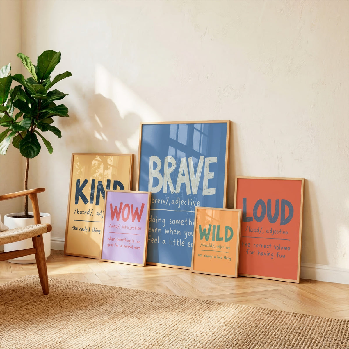 Five framed motivational art prints with colorful text are arranged on a light wood floor against a beige wall, next to a potted green plant and a wooden chair.