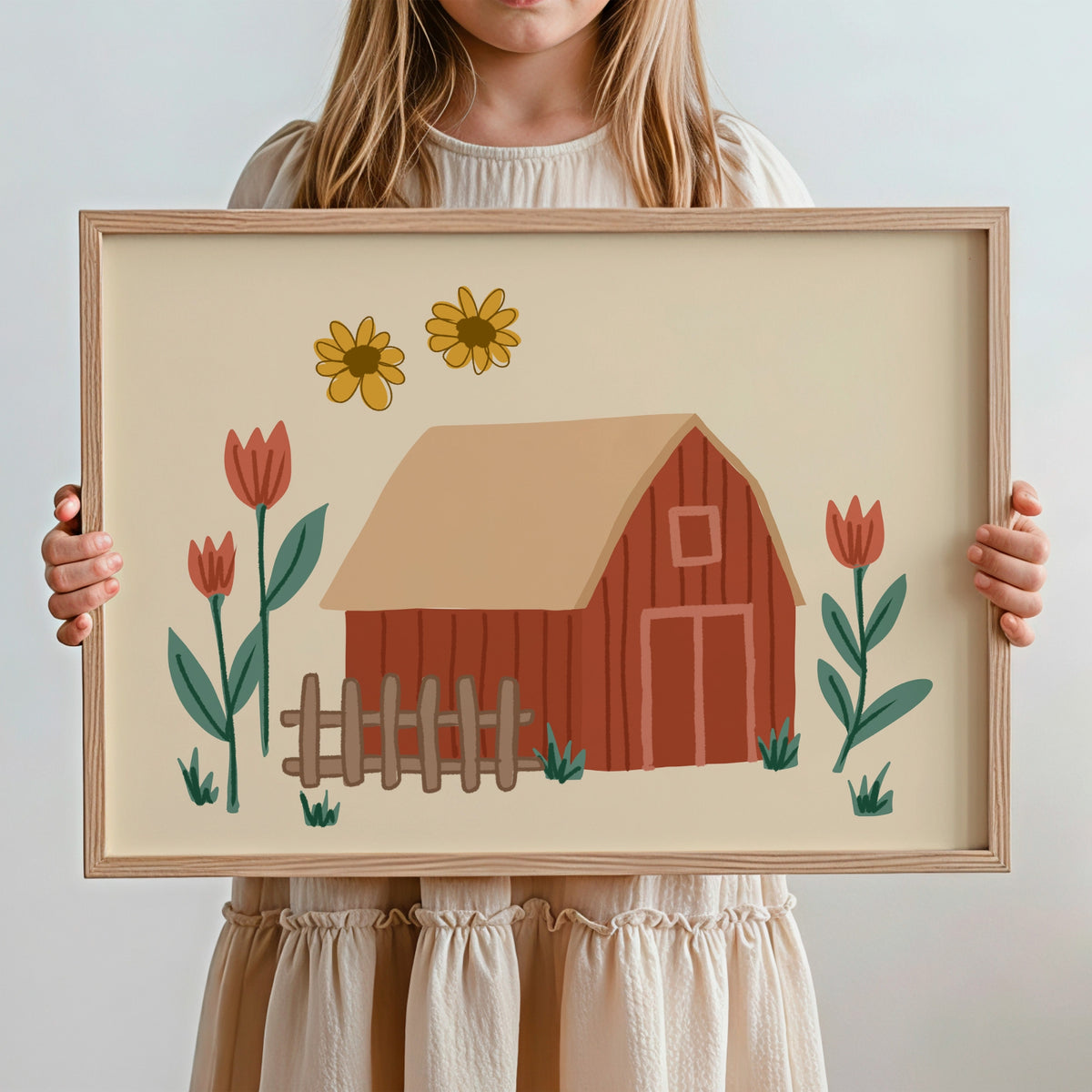 A child holds a framed art print featuring a whimsical barn illustration with flowers. The child is wearing a cream-colored dress, and the background is a clean, light gray studio wall.