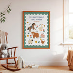 A framed children's educational poster titled 'OLD MACDONALD HAD A FARM' hanging on a white wall in a cozy, sunlit nursery. The poster features colorful cartoon farm animals like a horse, duck, sheep, pig, chicken, and cow on a green patterned background.