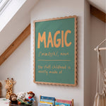 A framed educational wall sign with a scalloped wooden frame and a sage green chalkboard-style background, hanging on a white wall in a child's room. The sign features a dictionary definition of the word 'MAGIC' in orange lettering.