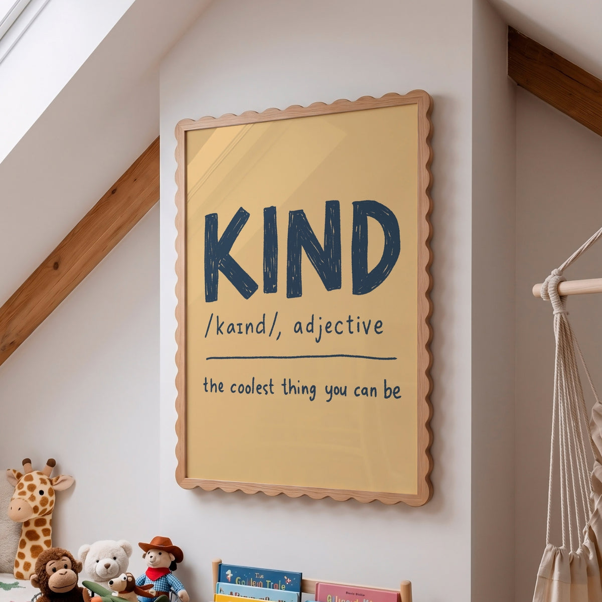 A framed educational wall poster with a scalloped wooden frame hangs on a white wall in a child's room. The poster features the word 'KIND' in large dark blue letters with its pronunciation '/kænd/, adjective' and the phrase 'the coolest thing you can be' written below.