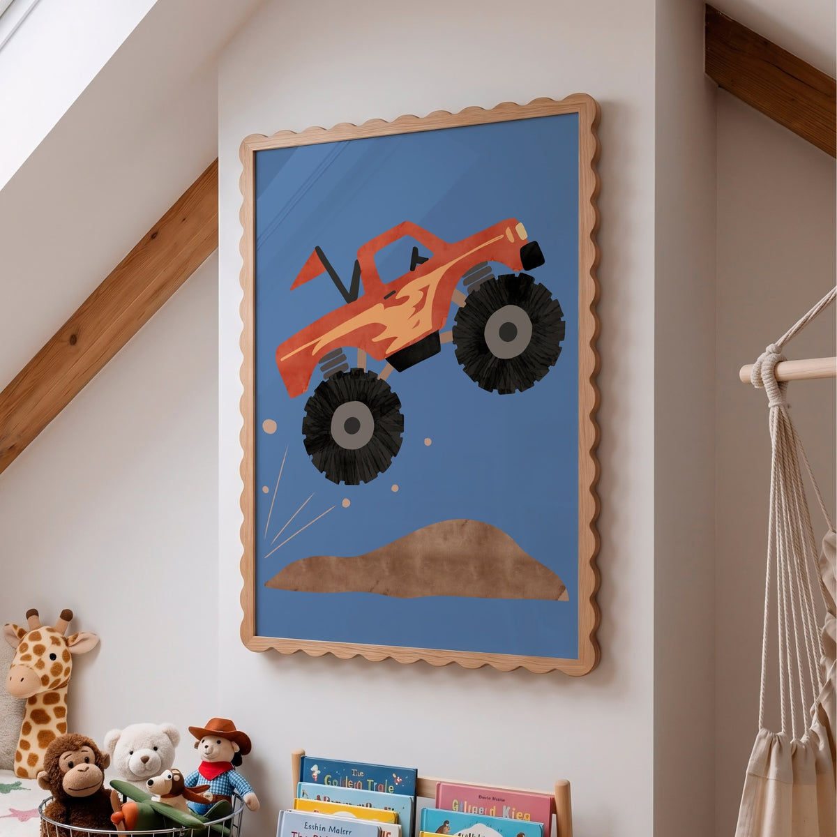 A framed children's wall art print featuring a cartoon orange monster truck jumping over a brown hill on a blue background, displayed on a white wall in a nursery or kids' room with toys and a hammock visible.
