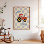 A framed children's wall art print hangs on a white wall in a nursery setting. The print features a red tractor with yellow wheels on a beige and gray checkered background, with the word 'BRUM' written above and below.
