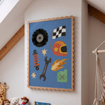 A framed art print featuring a blue background with various racing and workshop-themed icons like a checkered flag, tire, wrench, helmet, and flame, displayed on a white wall in a child's room.